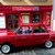 Roter klassischer Kombiwagen, der vor einem kleinen rot gestrichenen Laden mit dem Schild „Lila Samovar“ geparkt ist. Der Laden scheint russisch inspirierte Produkte oder Teeservice anzubieten.