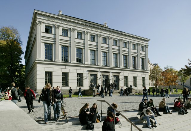 Großes klassizistisches Gebäude mit Säulen und vielen Fenstern, vor dem sich zahlreiche Menschen auf Stufen und im Freien aufhalten, vermutlich für eine Veranstaltung oder Demonstration.