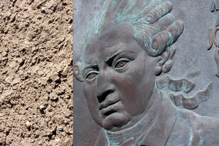 Bronzene Reliefplastik eines nachdenklich dreinblickenden Mannes mit lockigem Haar und markanten Gesichtszügen, vermutlich ein historischer Denker oder Künstler.