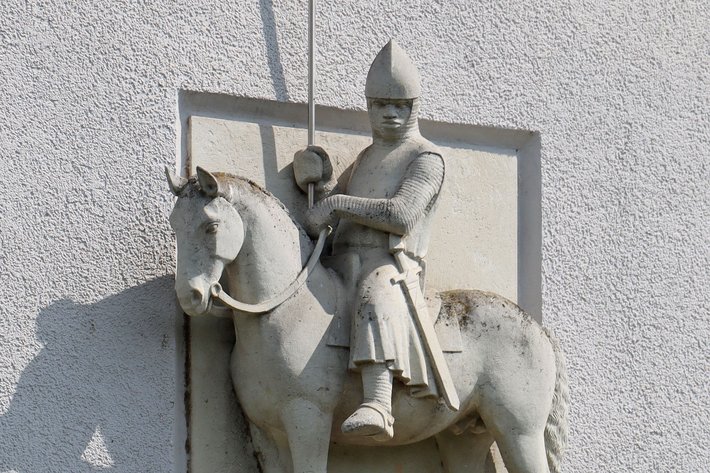 Ritterstatue auf einem Pferd, die mit mittelalterlicher Rüstung und Helm bekleidet ist, sitzt aufrecht im Galopp.