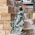 Bronzestatue einer sitzenden Frau, die Wasser aus einem Gefäß in einen kleinen Brunnen gießt, umgeben von spritzendem Wasser.