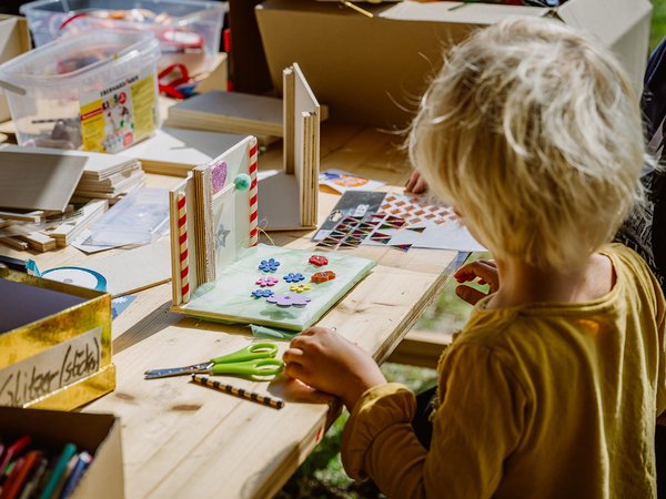 Ein Kind malt konzentriert an einem Tisch mit verschiedenen Malutensilien wie Stiften, Wasserfarben und Pinsel, umgeben von bunten Malvorlagen und Bastelmaterialien.