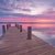 Holzstege führt bei Sonnenuntergang mit rosa und lila Himmel über ruhiges, spiegelndes Wasser ins Meer hinaus, friedliche Atmosphäre.