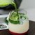 Glas mit cremigem grünem Smoothie oder Cocktail, der mit einer hellgrünen Flüssigkeit, vermutlich Limettensaft, beträufelt wird.