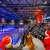 Große Eisbahn mit vielen Besuchern, die Schlittschuh laufen oder zuschauen. Einige tragen Weihnachtshüte und -mützen. Im Hintergrund eine beleuchtete Bühne mit Weihnachtsdekoration und dem Schriftzug „Rodelbahn“.