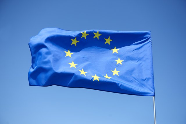 Blaues Flaggenfeld mit zwölf goldenen Sternen in Kreisformation, die im Wind weht – Symbol der Europäischen Union.