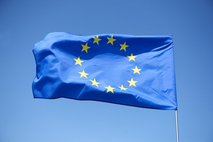 Blaues Flaggenfeld mit zwölf goldenen Sternen in Kreisformation, die im Wind weht – Symbol der Europäischen Union.