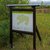 Schildertafel zeigt eine grüne Karte mit markiertem Wanderwegnetz im Naturpark, umgeben von Landschaft mit Hügeln und Grasland.