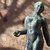 Bronzefigur eines nackten, jungen Mannes, der mit leicht angehobenem rechten Arm und nach vorne gerichtetem Blick steht.