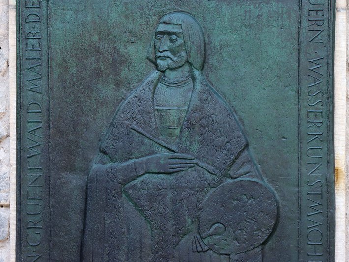 Bronzene Gedenktafel mit Relief eines sitzenden Mannes in traditioneller Kleidung, der eine Palette hält, symbolisch für den Maler Ernst Waldmüller.