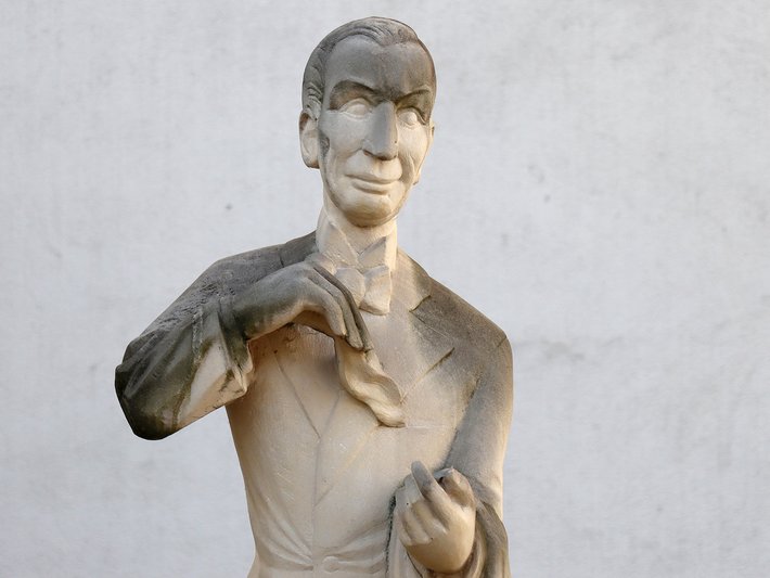 Bronzefigur eines Mannes mit kurz geschnittenem Haar, der mit beiden Händen eine Geste macht, als würde er etwas halten oder zeigen, in lockerem Stehpose.